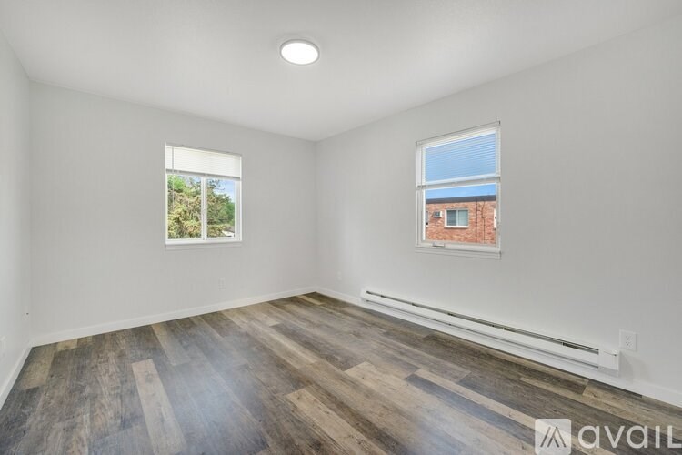 A room with wooden flooring and two windows.