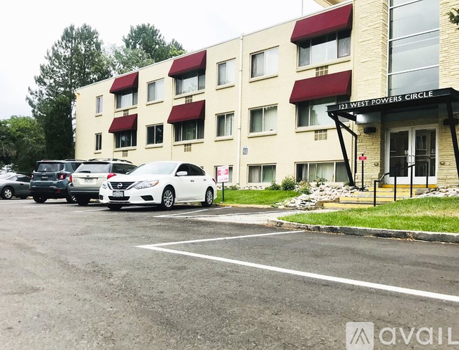 A white car is parked in front of a building with a sign that reads "123 WEST POWERS CIRCLE".