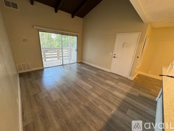 A room with wooden flooring and a sliding glass door leading to a balcony.