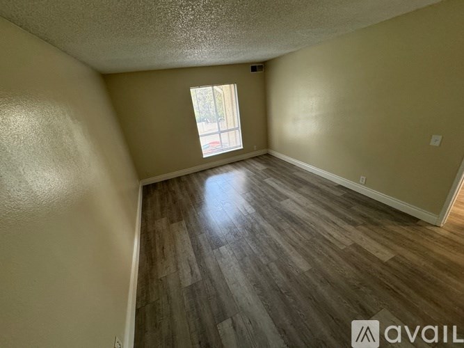 A room with wooden flooring and a window letting in sunlight.