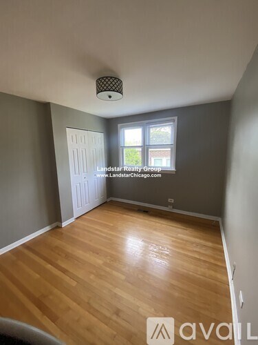 A room with wooden flooring and a window showing greenery outside.