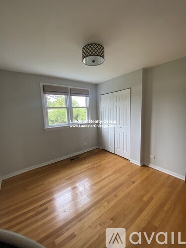 A room with wooden flooring and a window with a view of greenery outside.