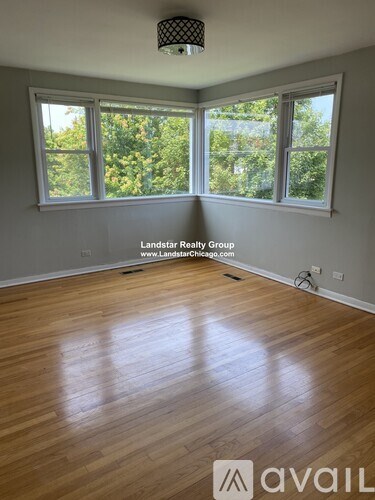A room with wooden flooring and a large window overlooking trees.