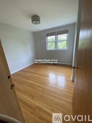 A room with wooden flooring and a window with a view of greenery outside.