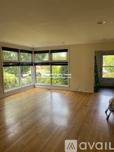 A room with wooden floors and a large window with a view of trees and a car.