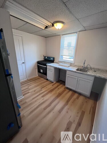 A kitchen with wooden floors and a fridge on the left.