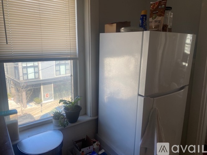 A white refrigerator stands in a kitchen next to a window with blinds.