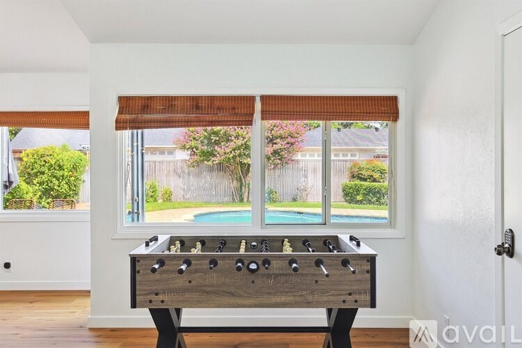 A foosball table sits in a room with a window overlooking a pool.