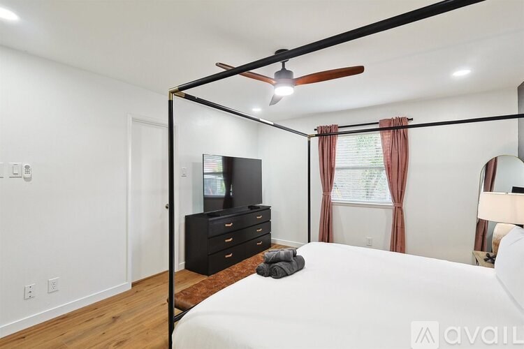 A bedroom with a four poster bed, a dresser and a ceiling fan.