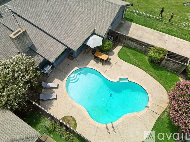 A swimming pool in a backyard surrounded by a concrete patio and a wooden deck.