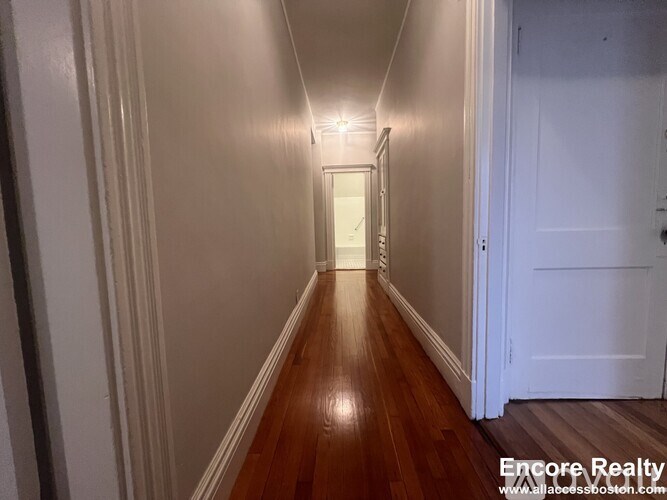 A long hallway with wood floors and white walls.