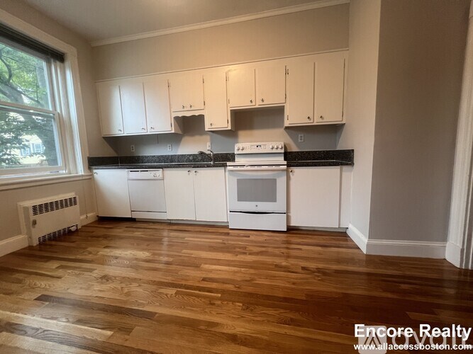 A kitchen with white cabinets and a wood floor.