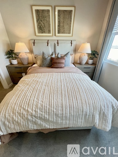 A bedroom with a bed, two nightstands with lamps, and a painting on the wall.