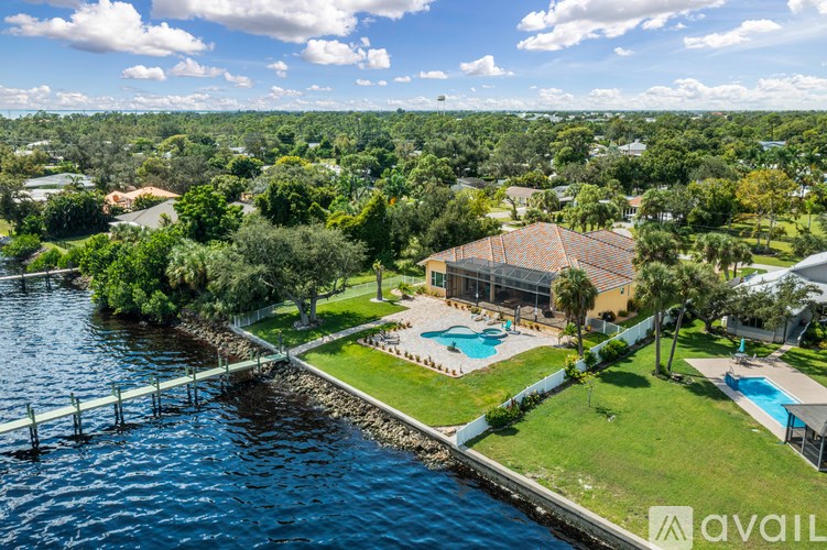 A house with a pool is surrounded by greenery and is located next to a body of water.