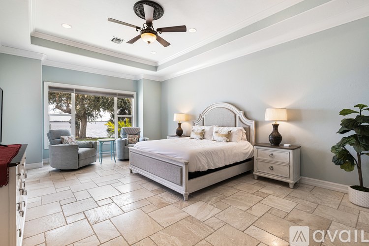 A bedroom with a large bed, a chair, a table, and a potted plant.