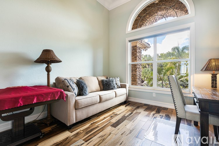 A living room with a couch, a table with a red cloth, and a large window with a view of trees.