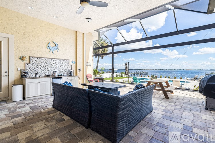 A patio with a black wicker sofa and a table with a glass roof over it.