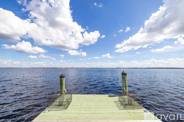 A pier extends into a calm body of water under a blue sky with scattered clouds.
