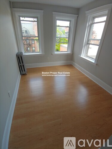 A room with wooden flooring and three windows.
