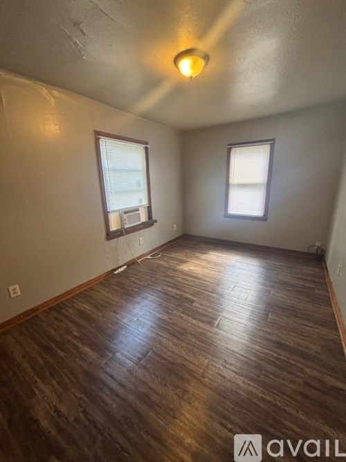 A room with wooden flooring and two windows.