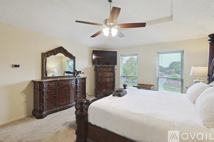 A bedroom with a large bed, a dresser with a mirror, and a ceiling fan.