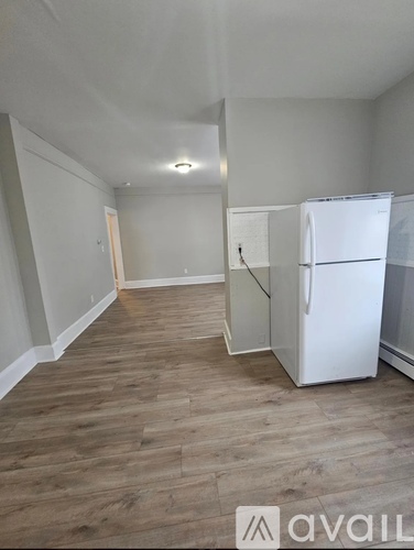 A white refrigerator is in a kitchen with wood flooring.