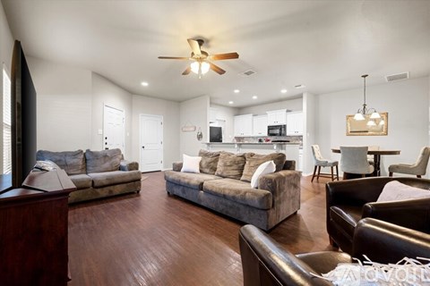 A spacious living room with a brown sofa set and a ceiling fan.