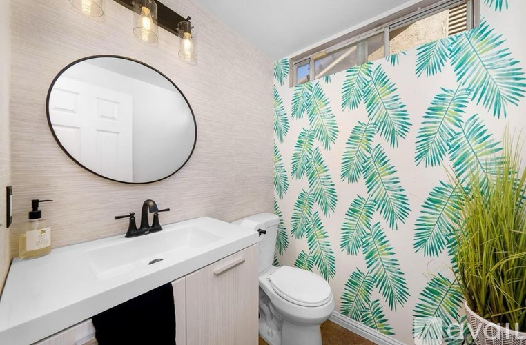 A bathroom with a white sink, toilet, and a mirror with a leaf pattern wallpaper.