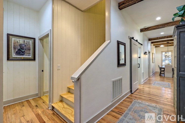 A hallway with a wooden floor and a staircase with a white railing.