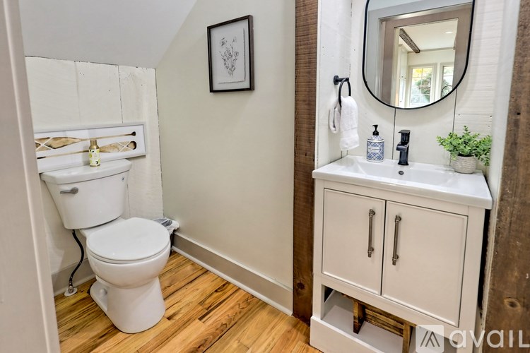 A white toilet is in a small bathroom with a wooden floor.