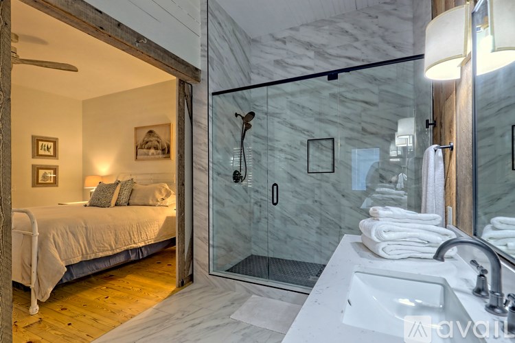 A bathroom with a marble wall and a bedroom with a bed and a window.