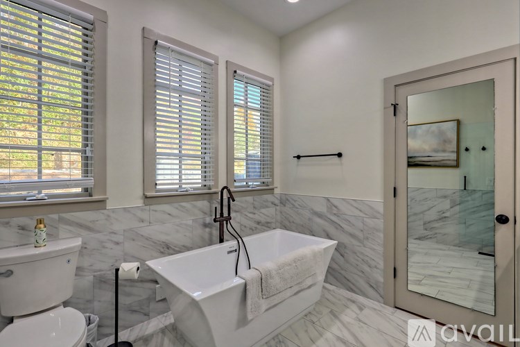 A bathroom with a white tub and sink, a toilet, and a window with blinds.