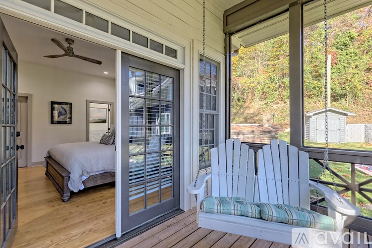 A white bedroom with a bed and a chair on the porch.