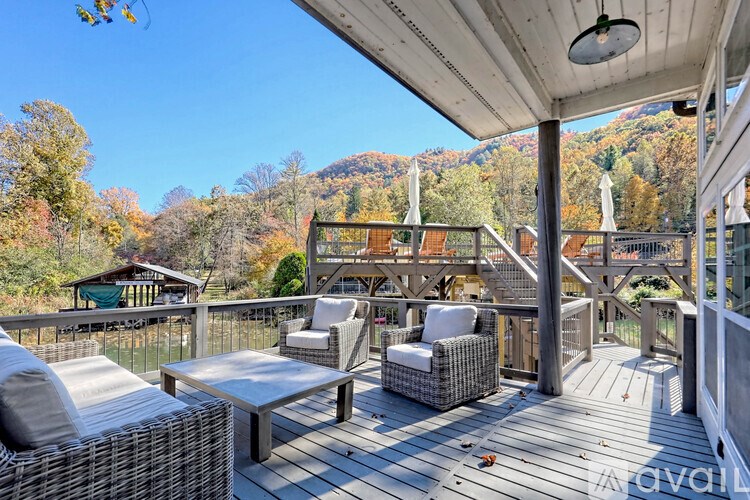 A wooden deck with chairs and a table is surrounded by a railing and trees.