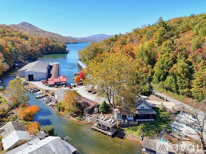 A serene landscape with a lake, houses, and autumn trees.