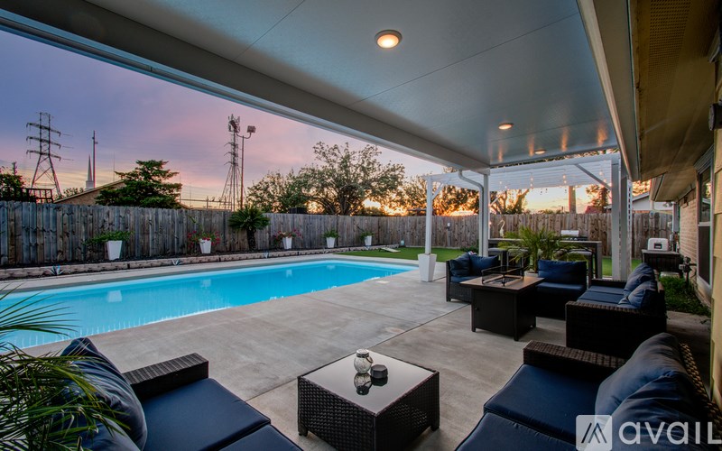 A pool surrounded by a patio with furniture and a fence.