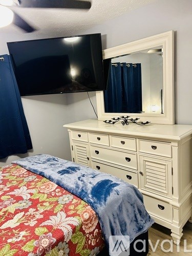 A bedroom with a floral bedspread and a white dresser with a mirror above it.