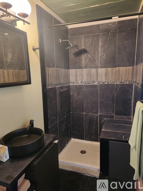 A bathroom with a black sink and a black tiled shower.
