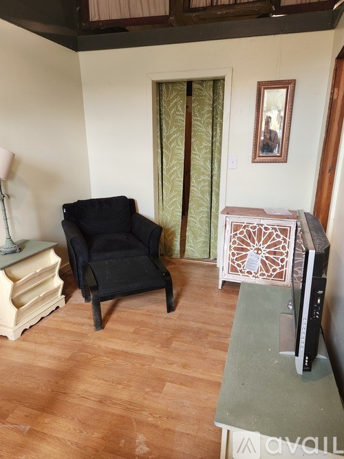 A living room with a black chair, a white side table, and a television.