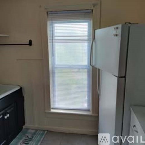 A white refrigerator stands in a kitchen next to a window with blinds.