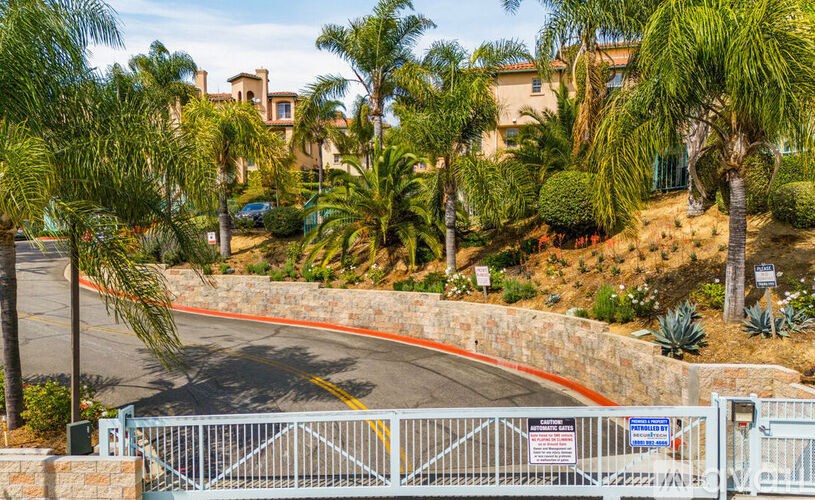 A gated entrance to a residential area with a road and palm trees.