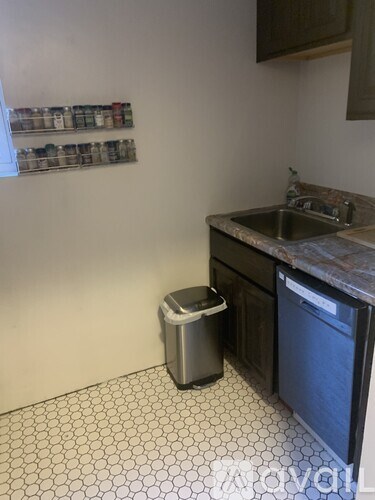 A kitchen with a black dishwasher and a white tiled floor.