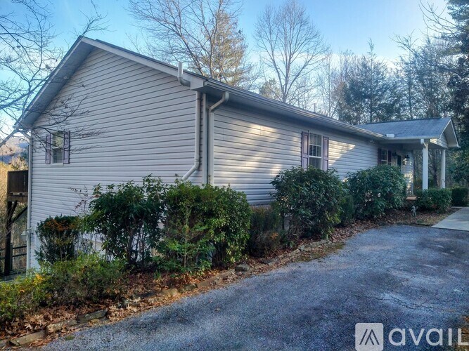A house with a grey siding and a white roof is surrounded by green bushes and trees.
