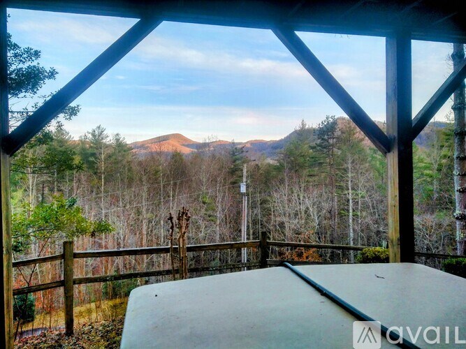 A wooden deck with a table and chairs overlooking a forest and a mountain.