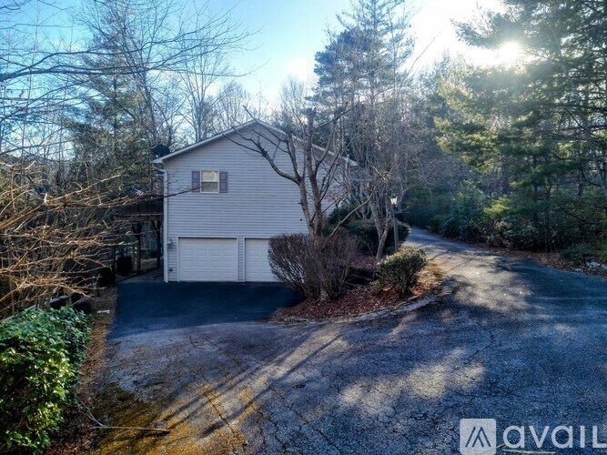 A house with a driveway and garage is surrounded by trees.