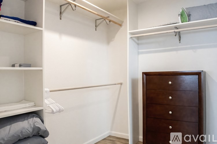 A white closet with a brown dresser and a white shelf.