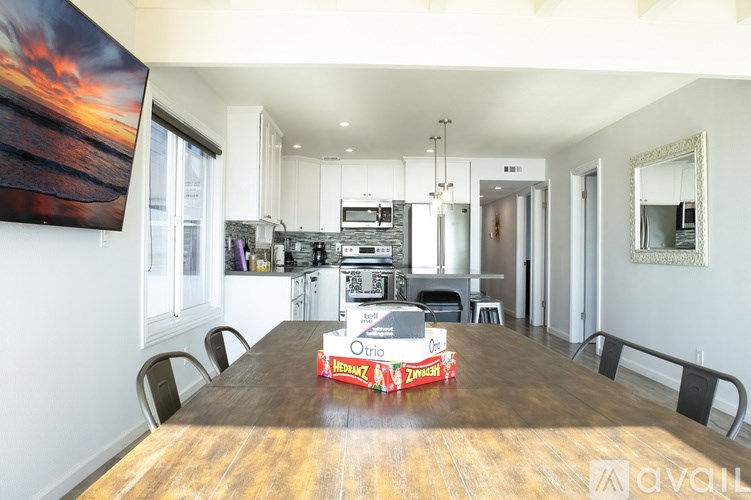 A kitchen with a wooden table and chairs in the foreground and a painting of a sunset on the wall.
