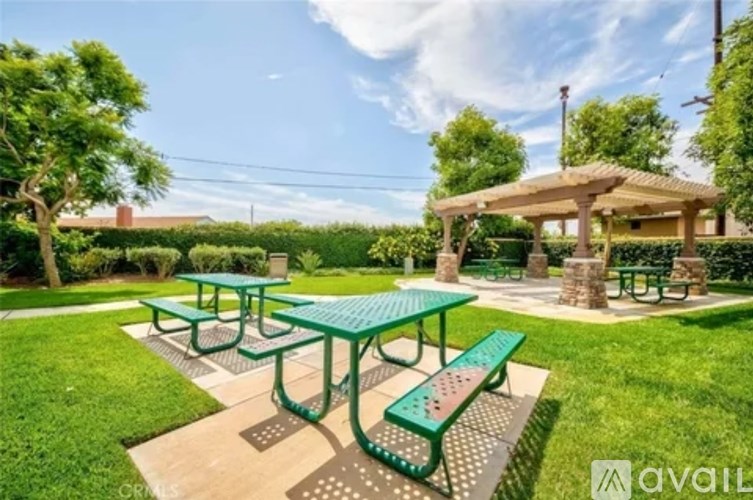 A green picnic table with a bench and a gazebo in a sunny park.
