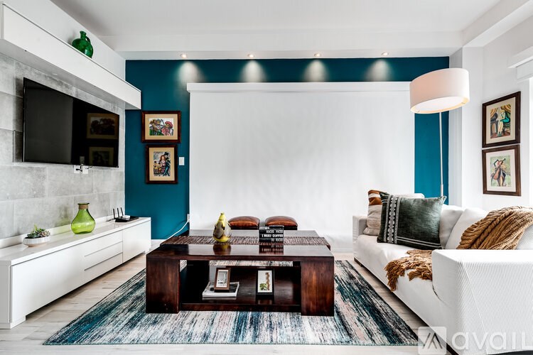 A living room with a white couch, a coffee table, and a flat screen TV mounted on the wall.