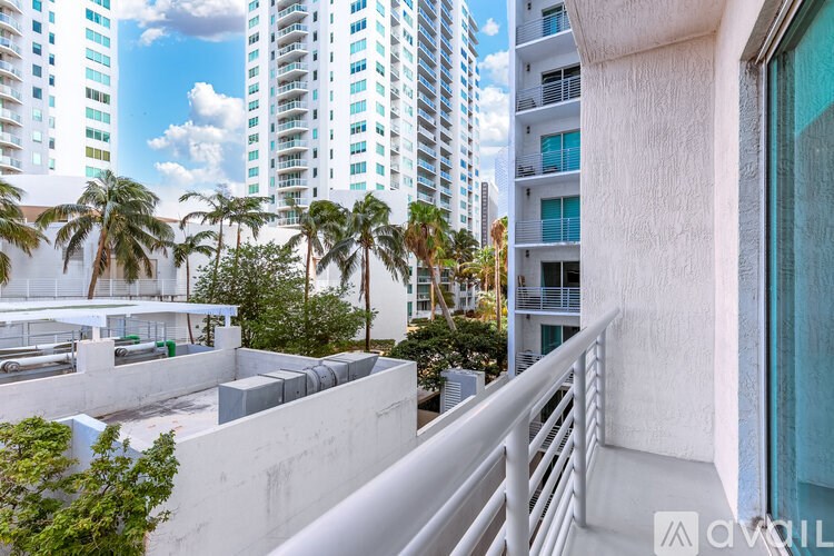 A balcony with a white railing overlooks a courtyard with palm trees and buildings in the background.